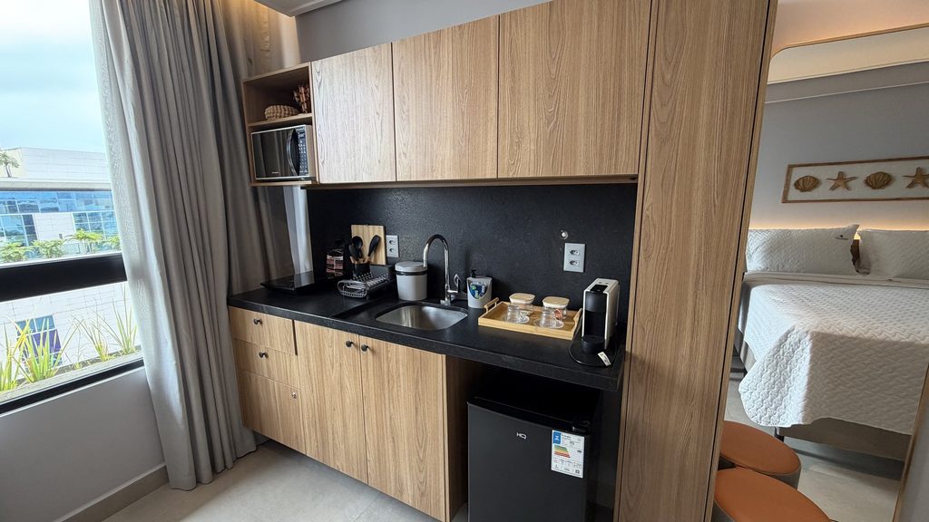 Cozinha compacta com marcenaria sob medida em madeira, bancada escura, frigobar e micro-ondas embutido